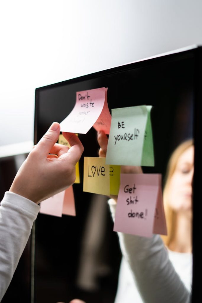 woman-in-white-long-sleeve-shirt-holding-sticky-note-3831844 A person placing colorful motivational sticky notes on a mirror for inspiration.